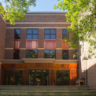 A modern brick building featuring large windows and surrounded by green foliage.