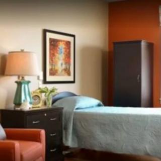 A cozy bedroom with a bed, nightstand, lamp, and painting.