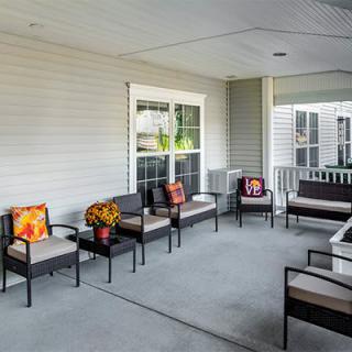 A cozy porch with multiple chairs and a table, decorated with colorful pillows.