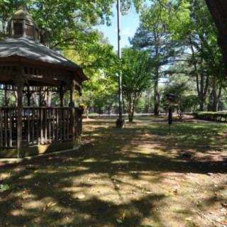A peaceful park scene with a gazebo, surrounded by trees and dappled sunlight.