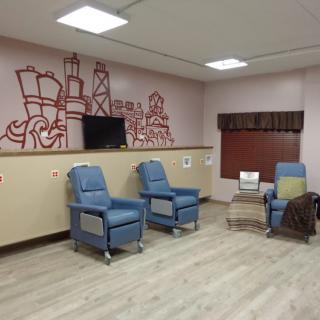 A medical treatment room with comfortable chairs and a television, decorated with wall art.