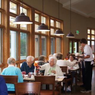 A group of seniors enjoying a meal together in a restaurant, attended by a waiter.