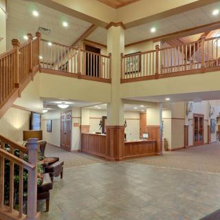A spacious hotel lobby with a reception desk, staircase, and wooden accents.