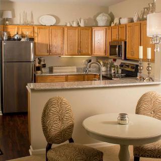 A modern apartment kitchen with wood cabinets and stainless steel appliances, featuring a cozy dining area.