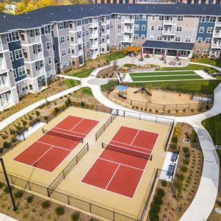Aerial view of a modern apartment complex with tennis courts and landscaped outdoor areas.