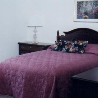 A neatly arranged bedroom with a purple quilt and floral pillows.