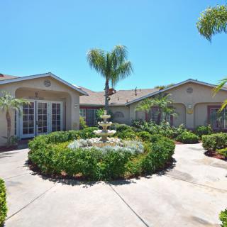 A beautiful house with a round driveway and central fountain surrounded by lush landscaping.