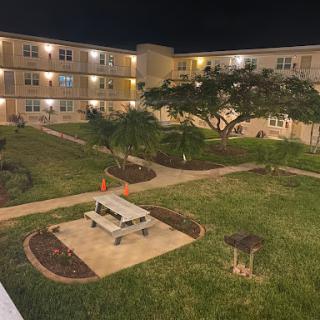 A serene view of an apartment complex courtyard at night, featuring a picnic area and lush landscaping.