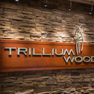 Illuminated Trillium Wood sign mounted on a stone wall.