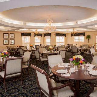 An elegant dining room with neatly arranged tables and chairs, decorated with flowers and chandeliers.