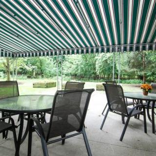 A cozy outdoor patio with tables and chairs under a green striped awning, surrounded by lush greenery.