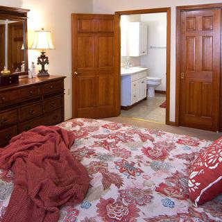 A cozy bedroom with a floral bedspread, wooden dresser, and an open door leading to a bathroom.