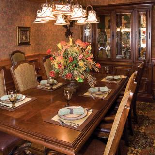 An elegantly set dining room table with a floral centerpiece and a chandelier overhead.