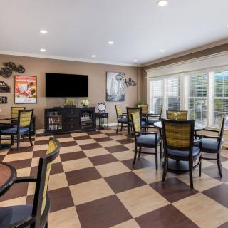 A community dining area with checkered flooring, tables and chairs, a large television, and wall decorations.