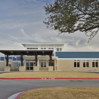 A modern school building with a blue and beige facade under a cloudy sky.