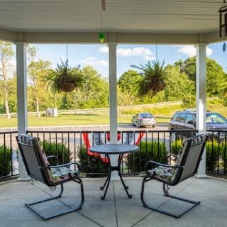 A cozy outdoor porch with two chairs and a table, surrounded by greenery.