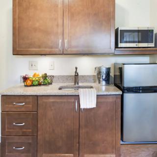 A compact kitchen space with wooden cabinets, a small refrigerator, a microwave, and a countertop with a fruit bowl.