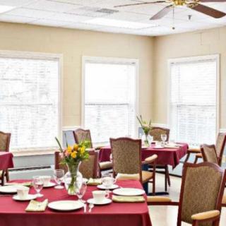 A well-lit dining room with tables set for a meal, featuring red tablecloths, elegant dishware, and floral centerpieces.