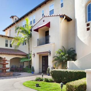 A sunny view of a modern residential apartment building with palm trees and well-maintained landscaping.