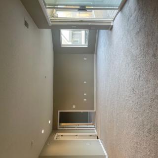 An empty room with beige carpeting, recessed lighting, and large windows offering natural light.