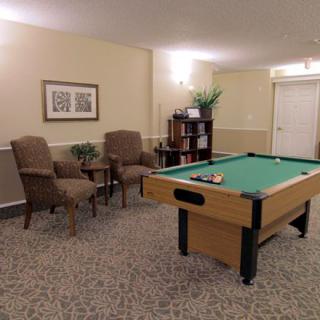 A cozy game room featuring a pool table, comfortable chairs, and a bookshelf.