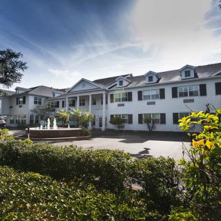 A large residential building with classic architectural features, surrounded by greenery and set against a clear sky.