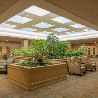 A spacious lobby area with comfortable seating and lush indoor plants under a skylight.