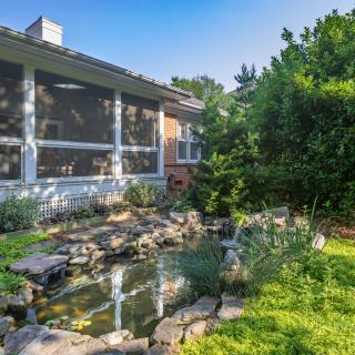 A serene backyard featuring a pond surrounded by lush greenery and a screened porch on the house.