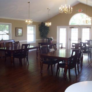 A well-lit dining room with tables and chairs arranged neatly, featuring chandeliers and large windows.