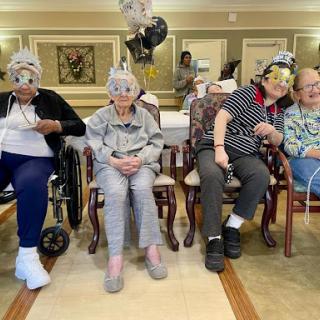 A joyful gathering of seniors celebrating together in a community center, wearing festive party hats and surrounded by balloons.