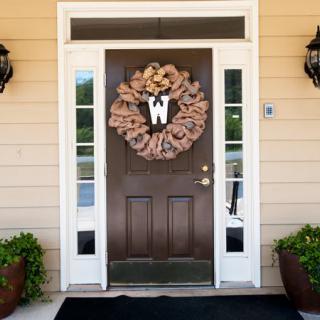 A front door decorated with a large wreath and flanked by plants.