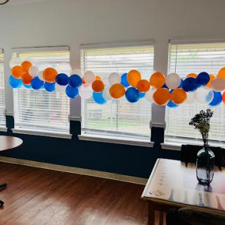 A festive display of orange, blue, and white balloons decorating a sunny indoor space.