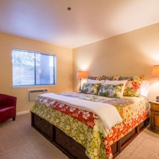 A cozy bedroom with a colorful bedspread, bedside lamps, and a window letting in natural light.