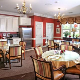 A warm and inviting kitchen and dining area featuring elegant chandeliers, round tables with striped chairs, and well-organized cabinets.