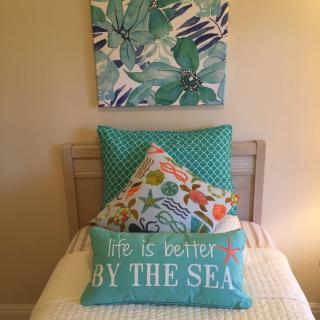 A cozy bedroom setup with coastal-themed pillows and artwork.
