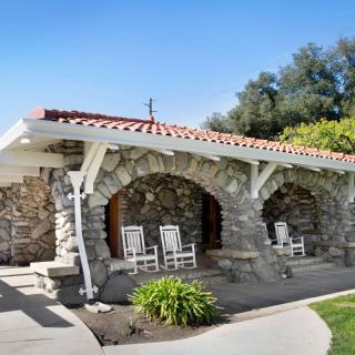 A charming stone house with a cozy porch featuring rocking chairs, surrounded by greenery.