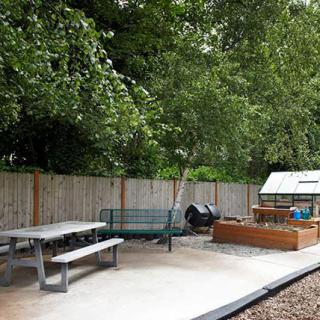 A peaceful garden area with a picnic table, bench, planters, and a small greenhouse.