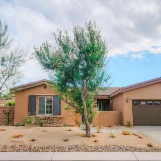 A single-story house with a garage and desert landscaping under a cloudy sky.