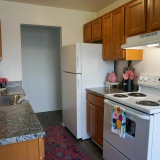 A compact kitchen with wooden cabinets, a refrigerator, stove, and granite countertops.