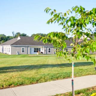 A residential building with a neatly maintained yard and sidewalk, featuring young trees and lush grass.