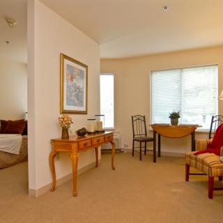 A cozy living room area with a table, chairs, and decorative elements, leading to a bedroom.