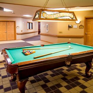 A well-lit game room featuring a pool table with cue sticks and balls ready for play.