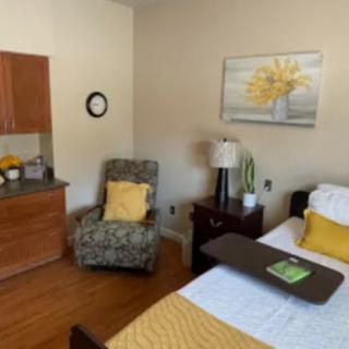 A cozy bedroom with a bed, armchair, and warm yellow accents.