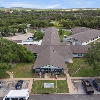 Aerial view of a multi-unit building surrounded by greenery and a parking area.