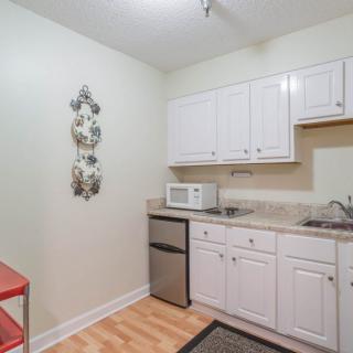 A compact kitchen featuring white cabinets, a microwave, mini fridge, and decorative plates on the wall.