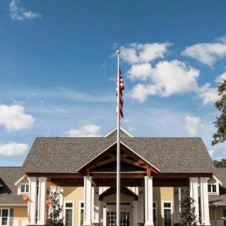 A building with a triangular roof entrance and a flagpole displaying the American flag against a blue sky with scattered clouds.