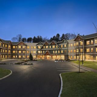 A well-lit hotel building at night with a spacious parking lot in front.