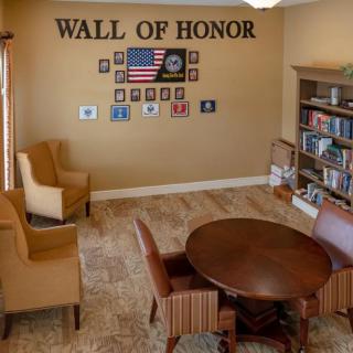 A room with a 'Wall of Honor' featuring military photos, armchairs, and a bookshelf.