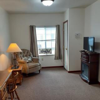 A cozy living room with a chair, desk, lamp, and television.