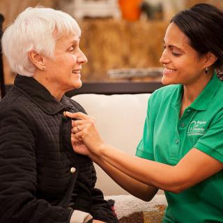 A caregiver assisting an elderly woman with her clothing.